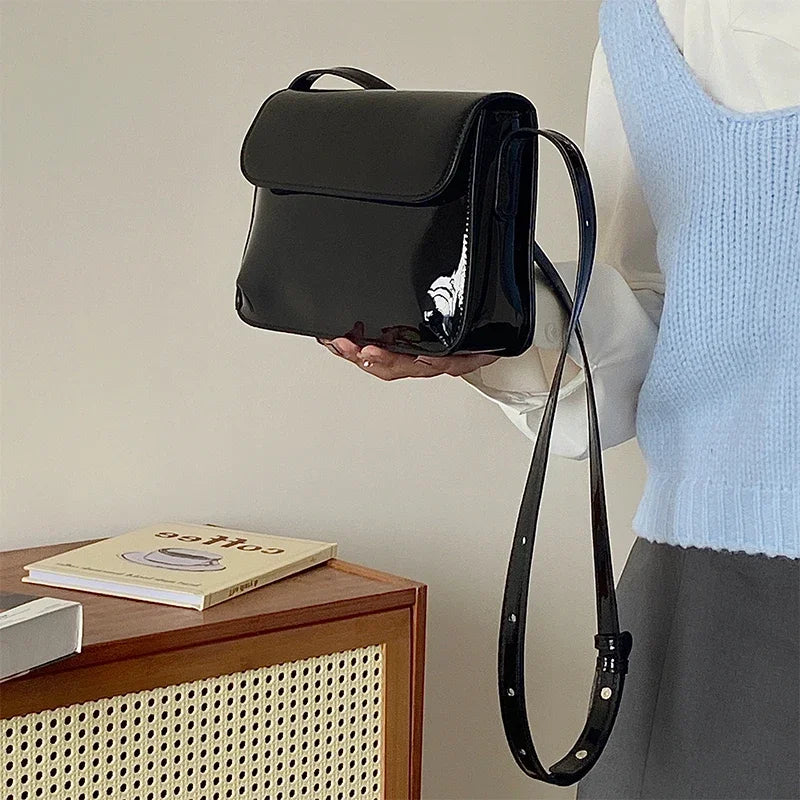 Frau hält schwarze, glänzende Umhängetasche aus Leder, modisch, elegant, Damenaccessoire.