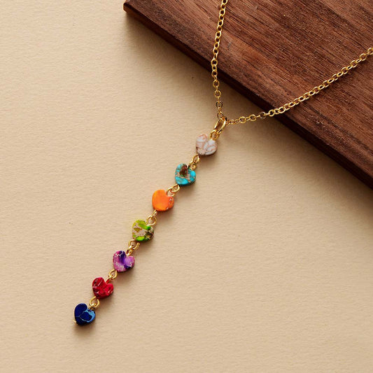 Goldene Halskette mit bunten Herzanhängern, Regenbogenfarben, auf Holzuntergrund.