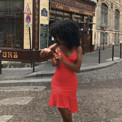 Frau in rotem Sommerkleid auf Kopfsteinpflasterstraße vor Café in Paris.