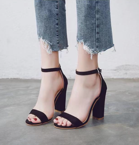 Frau trägt schwarze High Heels mit Blockabsatz und Knöchelriemen, zerrissene Jeans.
