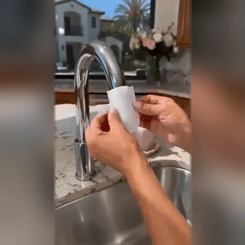 Två händer viker ett vitt filterpapper vid en krom-kran över en diskho med granit-bänk. 2