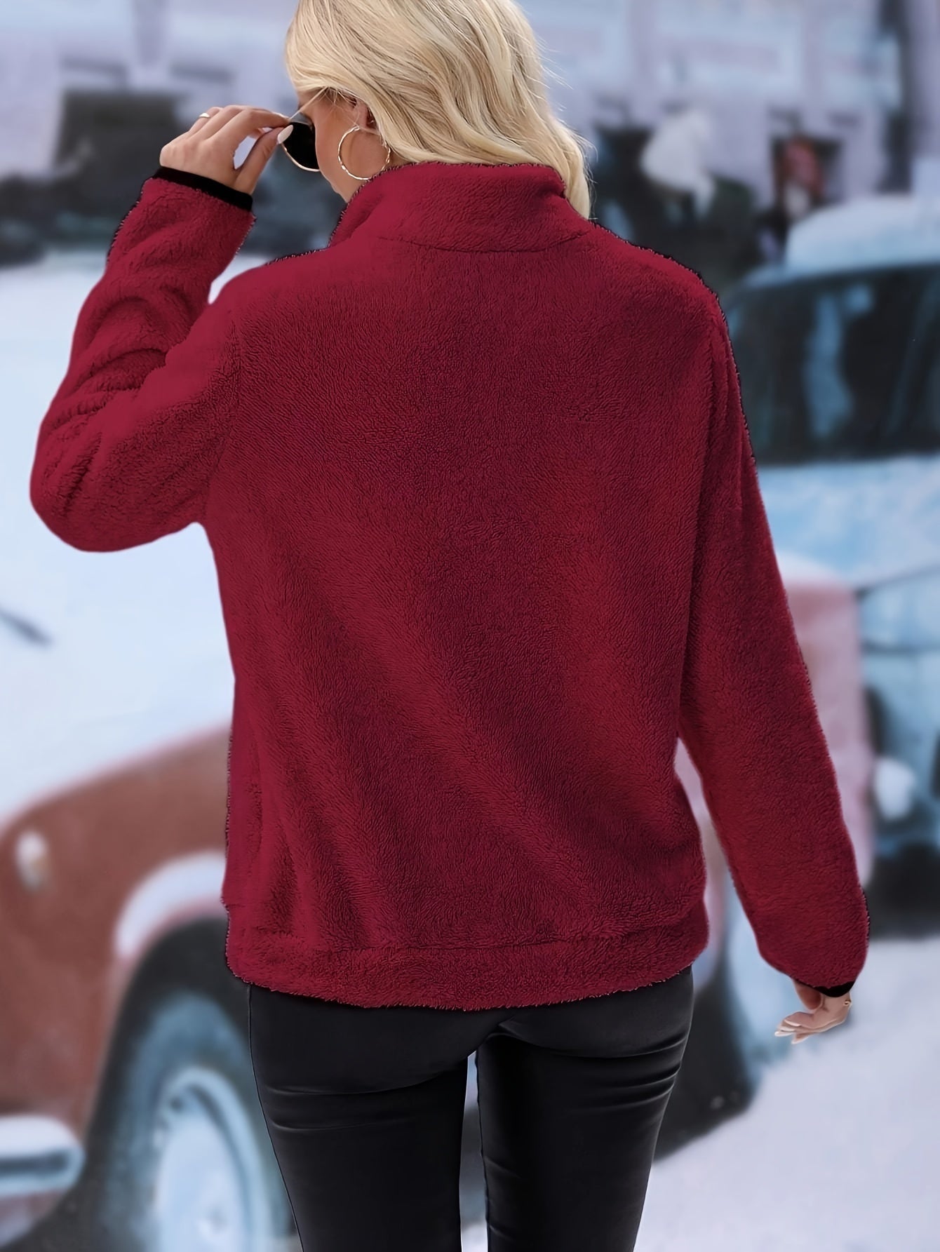 Frau in rotem Fleece-Pullover, schwarze Lederhose, Wintermode, Rückansicht, urbaner Hintergrund.