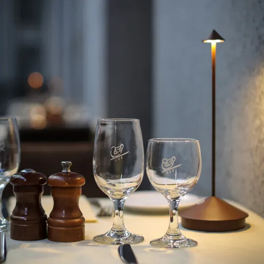 Zwei Weingläser auf gedecktem Tisch mit Salz- und Pfefferstreuer, moderne Tischlampe.