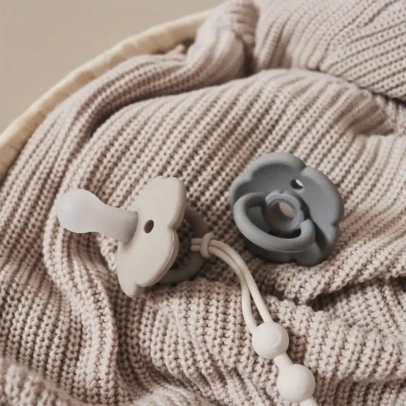 Beige Babydecke mit grauem und weißem Silikon-Schnuller auf Strickstoff.
