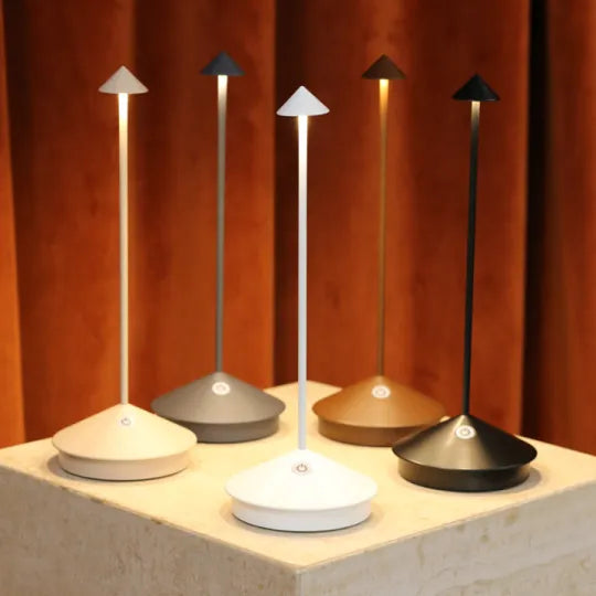 Fünf moderne LED-Tischlampen in verschiedenen Farben auf einem Podest vor braunem Vorhang.