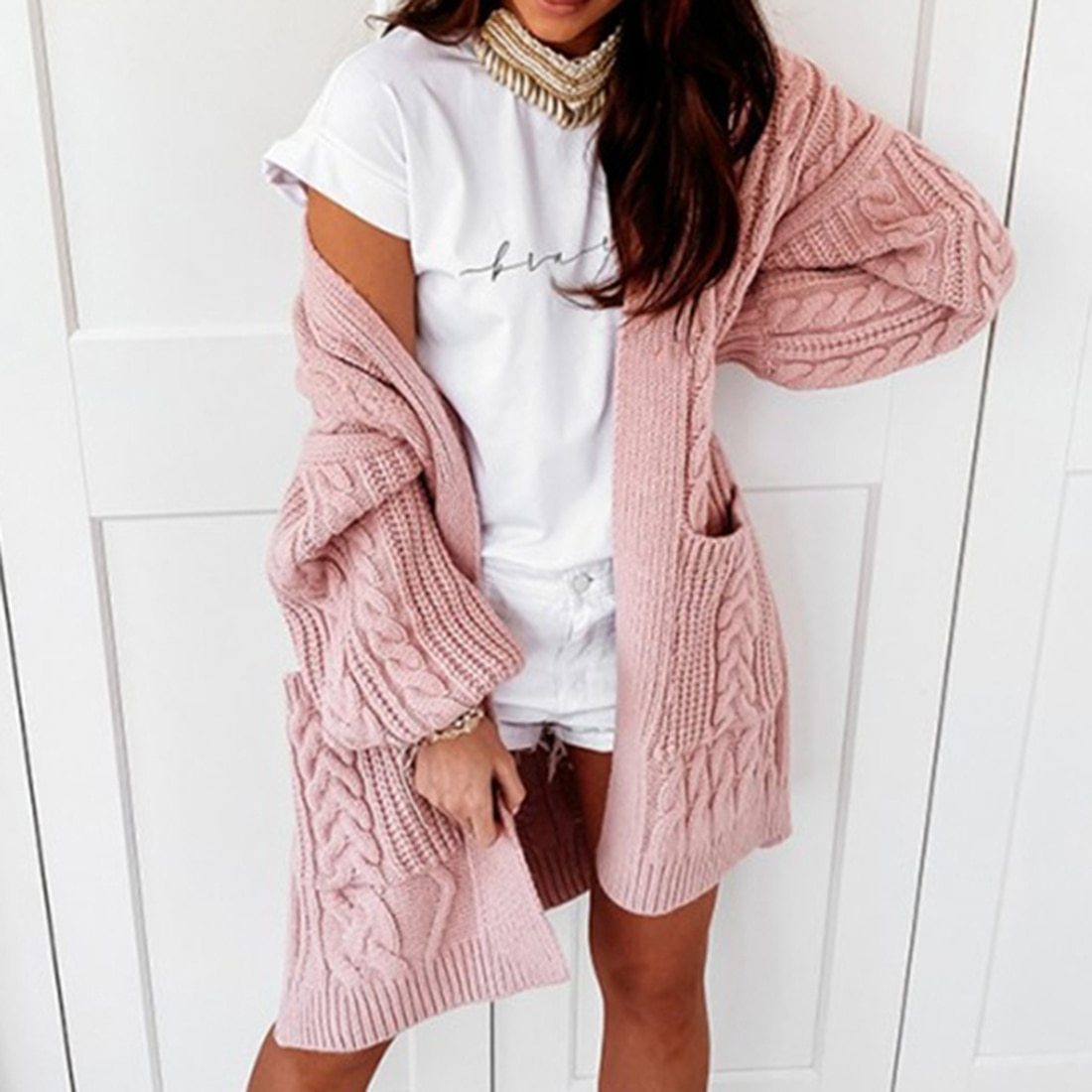 Frau trägt rosa Strickjacke, weißes T-Shirt, Shorts; modische Damenbekleidung, lässiger Look.