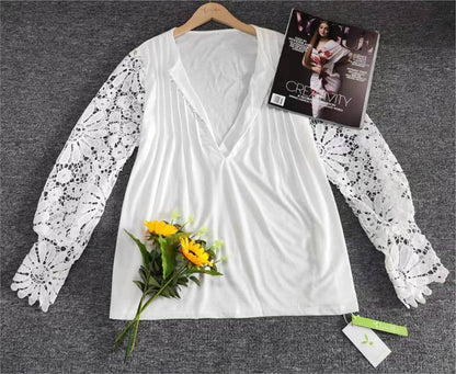 Weiße Bluse mit Spitzenärmeln, V-Ausschnitt, auf grauem Hintergrund, neben Sonnenblumen.