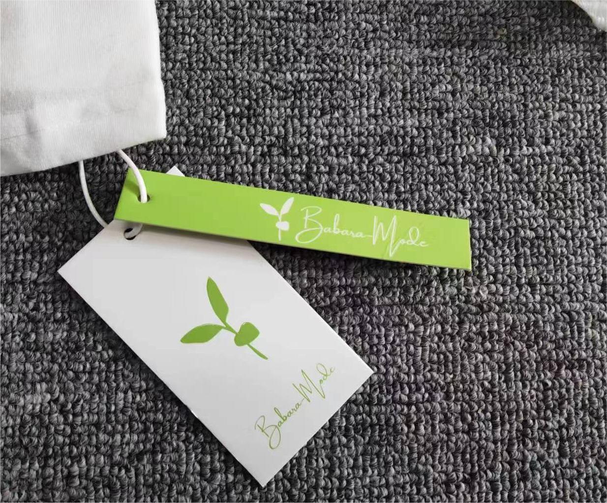 Weiße Stofftasche mit grünem Etikett, Barbara Mode Logo, auf grauem Teppich.