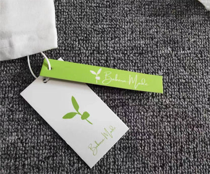 Weiße Stofftasche mit grünem Etikett, Barbara Mode Logo, auf grauem Teppich.