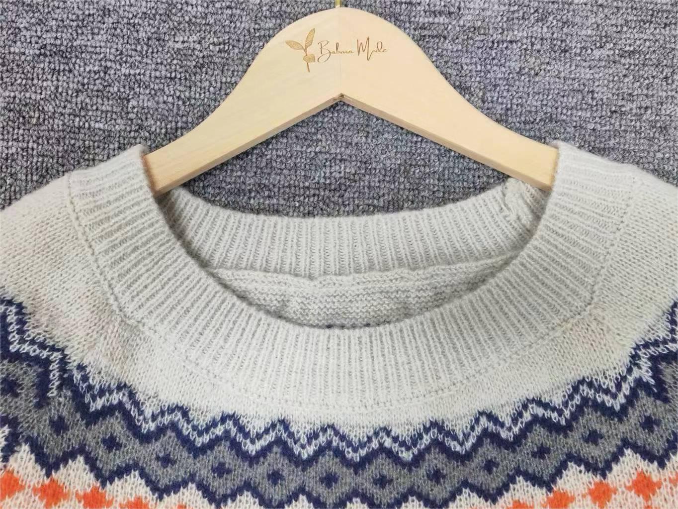 Grauer Strickpullover mit buntem Zickzackmuster auf Holzkleiderbügel.