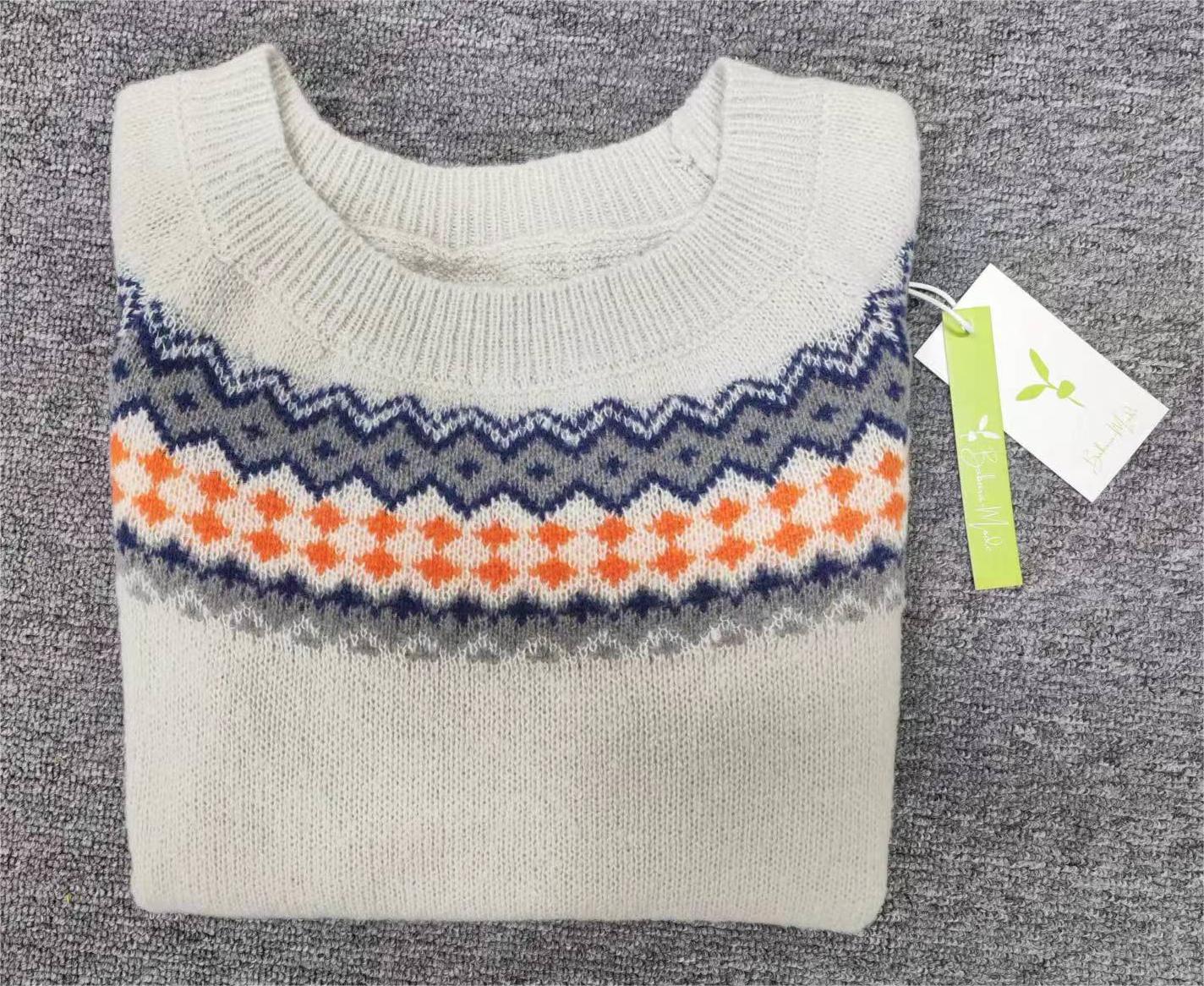 Beigefarbener Strickpullover mit blau-orangefarbenem Zickzackmuster auf grauem Hintergrund.