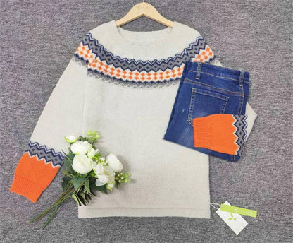 Grauer Strickpullover mit orange-blauem Muster, blaue Jeans, weiße Blumen, auf grauem Hintergrund.