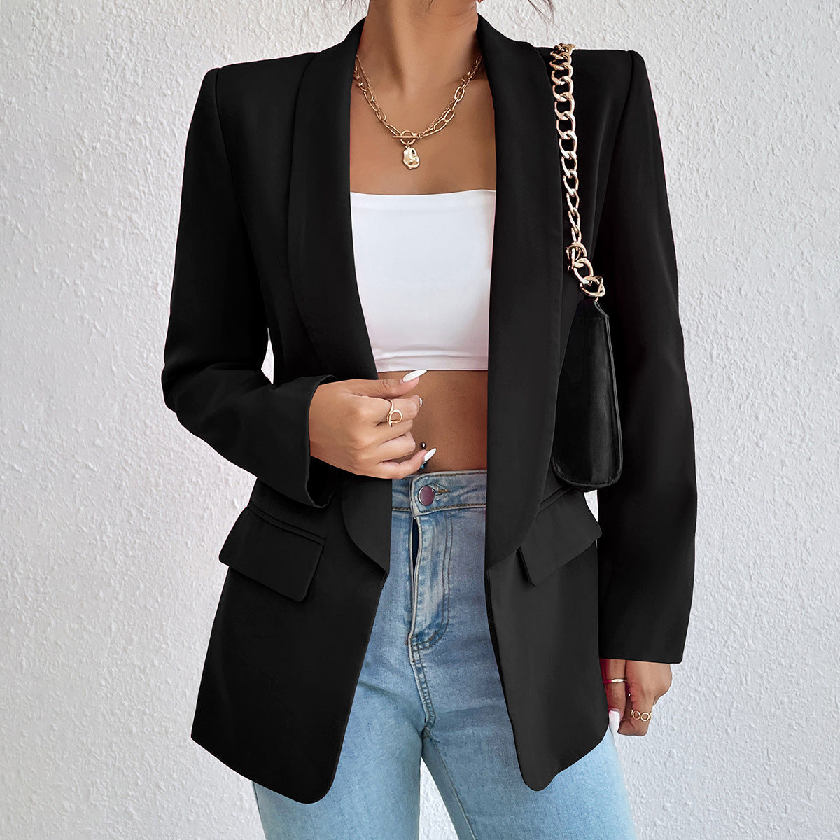 Frau in schwarzem Blazer, weißem Top, Jeans, mit schwarzer Tasche und Goldkette.