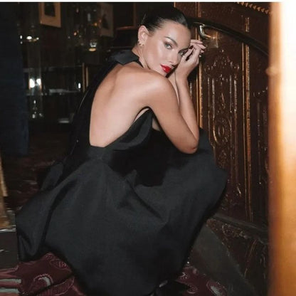 Frau in elegantem, schwarzem Abendkleid mit offenem Rücken, sitzt auf Treppe, glamouröses Ambiente.