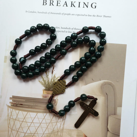 Dunkelgrüner Rosenkranz mit Kreuzanhänger, Holzperlen, religiöses Schmuckstück auf Tisch.