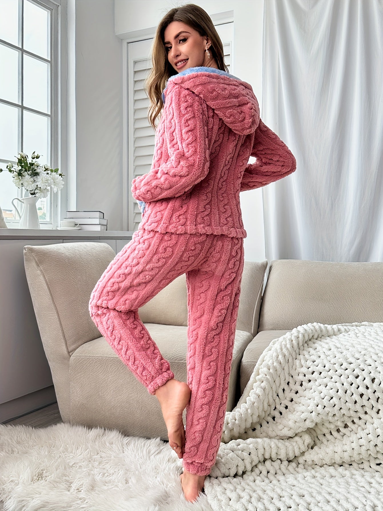 Frau in rosa Strick-Pyjama-Set, gemütlich, Wohnzimmer, Sofa, Fenster, Innenraum.