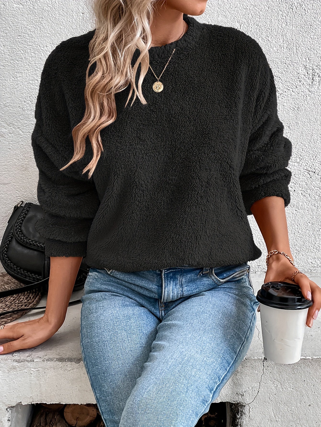 Frau in schwarzem Fleece-Pullover, blaue Jeans, hält Kaffeebecher, modisch, lässig, Herbstoutfit.