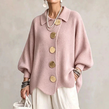 Rosa kofta i ribbstickat med stora guldfärgade knappar och vågig nederkant, buren med vita byxor och en flätad väska. 6