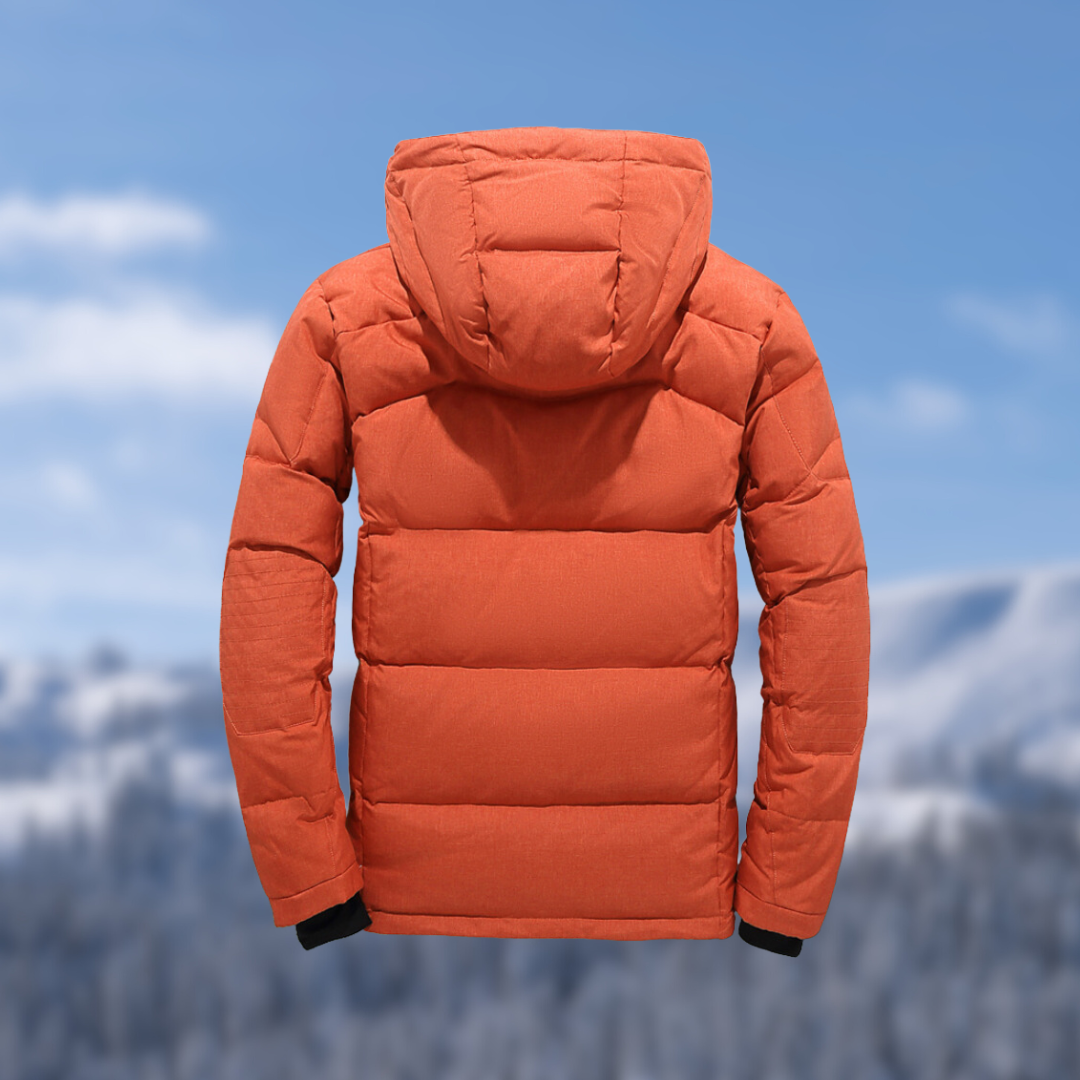 Orangefarbene Daunenjacke mit Kapuze, Wintermode, isoliert vor verschneiter Berglandschaft.