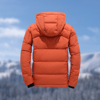 Orangefarbene Daunenjacke mit Kapuze, Wintermode, isoliert vor verschneiter Berglandschaft.