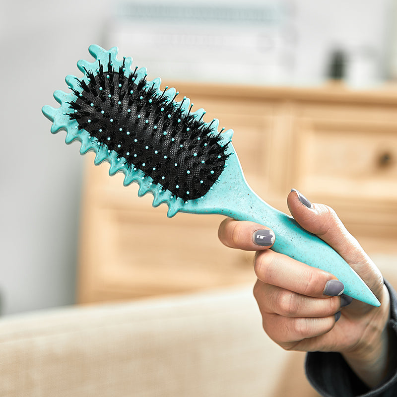 Hand hält türkisfarbene Haarbürste mit schwarzen Borsten, ergonomisches Design, Haarpflege.
