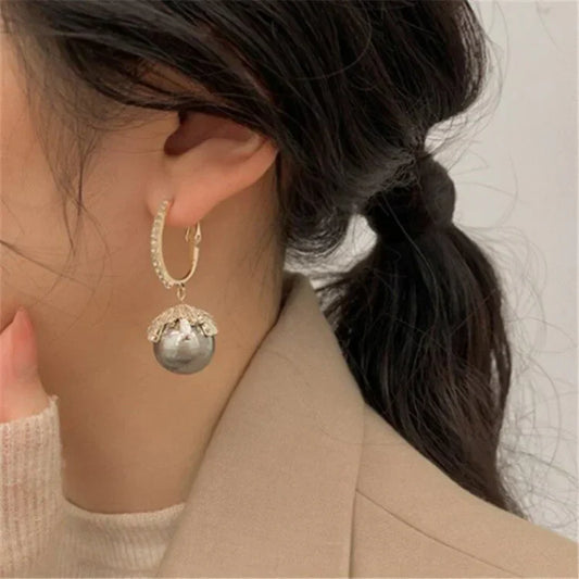 Frau mit schwarzem Haar trägt goldene Ohrringe mit großer grauer Perle, eleganter Schmuck.