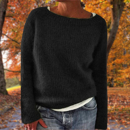 Svart stickad tröja med rund hals, bärd av en modell över vitt linne och jeans med lövfärgad höstpark i bakgrunden. 2