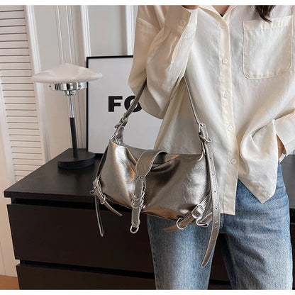 Frau mit silberner Lederhandtasche, weißer Bluse, Jeans, moderne Inneneinrichtung.