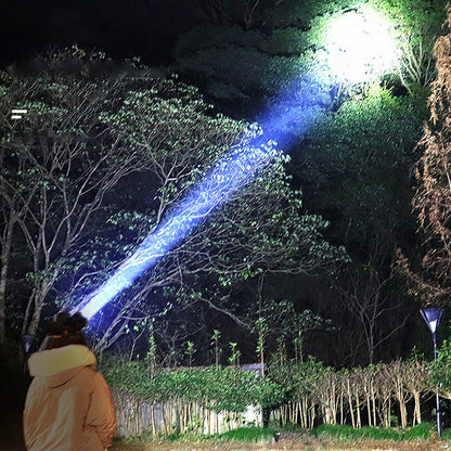 Person mit starker LED-Taschenlampe beleuchtet Baum im Wald bei Nacht.