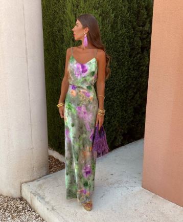 Frau im langen, floralen Sommerkleid mit lila Quasten-Ohrringen und passender Tasche.