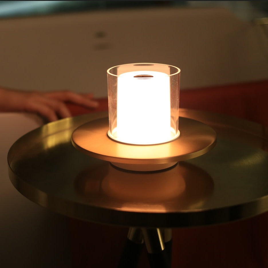 Moderne Tischlampe aus Glas und Metall auf rundem Tisch, warmes Licht, stilvolle Inneneinrichtung.