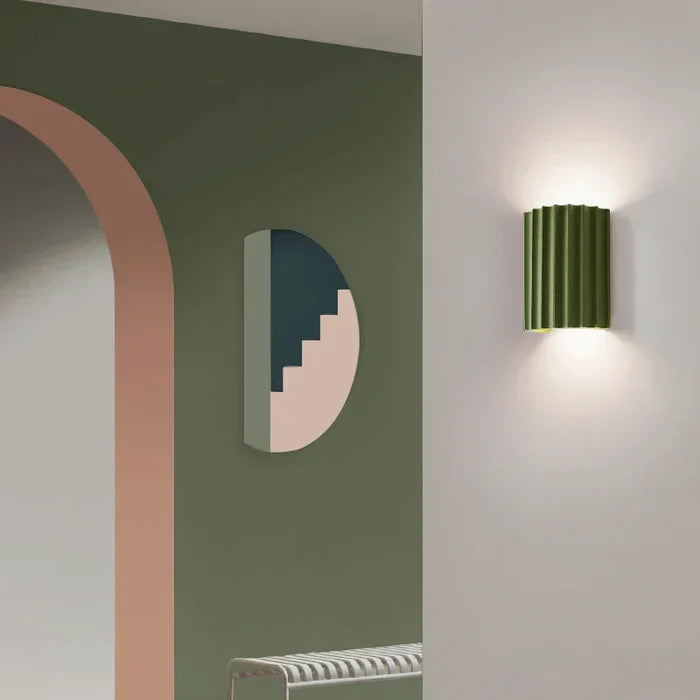 Grüne Wandleuchte im modernen Design, beleuchtet, neben geometrischer Wanddekoration.