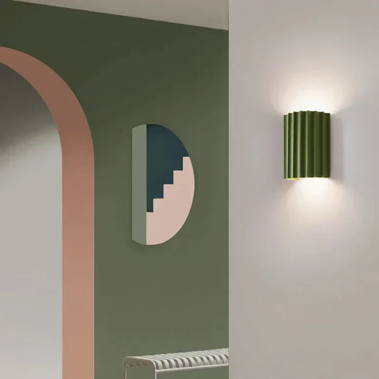 Grüne Wandleuchte im modernen Design, beleuchtet, neben geometrischer Wanddekoration.