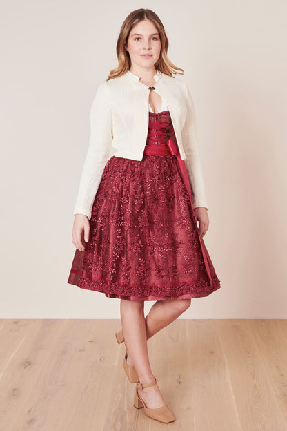 Frau in rotem Spitzenkleid und weißer Strickjacke, elegante Mode, Holzfußboden.