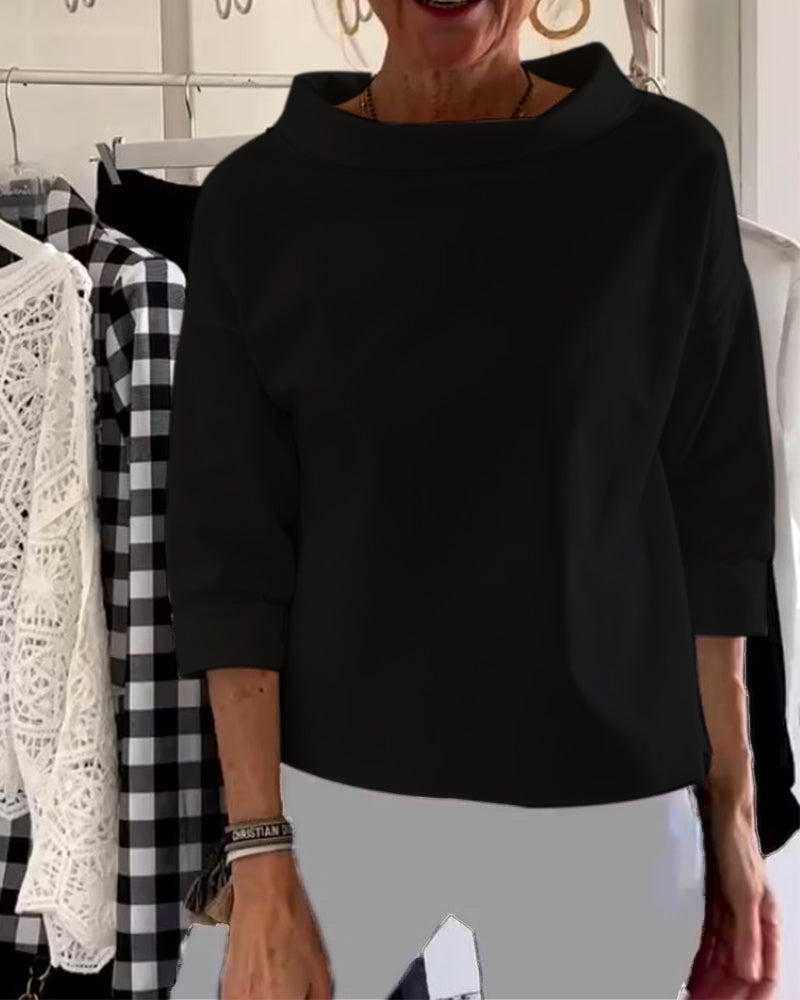 Frau in schwarzem Pullover, 3/4-Ärmel, vor kariertem und Spitzenkleidungsstück im Hintergrund.