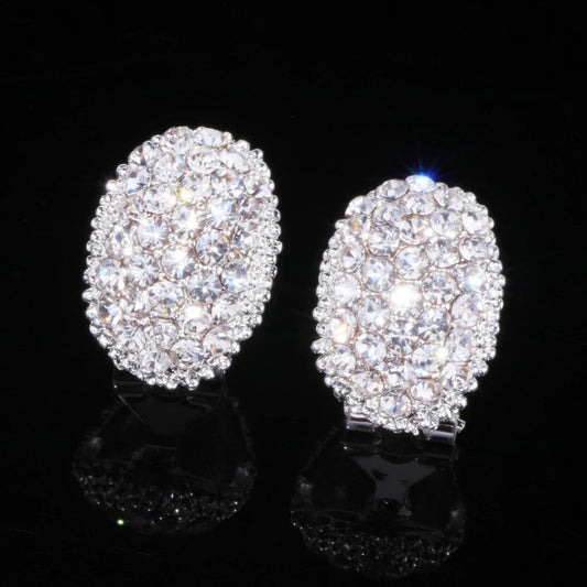 Ovale silberne Ohrringe mit Kristallsteinen, funkelnd, eleganter Schmuck, schwarzer Hintergrund.