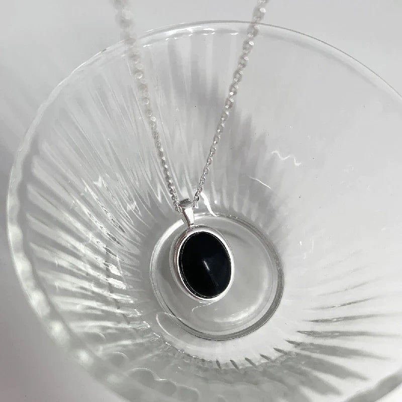 Silberne Halskette mit schwarzem ovalem Anhänger, elegantes Schmuckstück, Damenaccessoire.