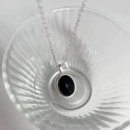 Silberne Halskette mit schwarzem ovalem Anhänger, elegantes Schmuckstück, Damenaccessoire.