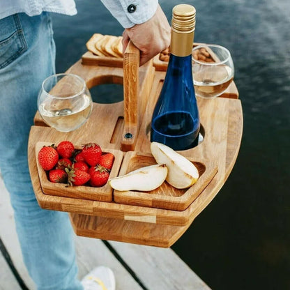 Tragbarer Picknicktisch aus Holz mit Weinflasche, Gläsern, Erdbeeren und Birnen am Seeufer.