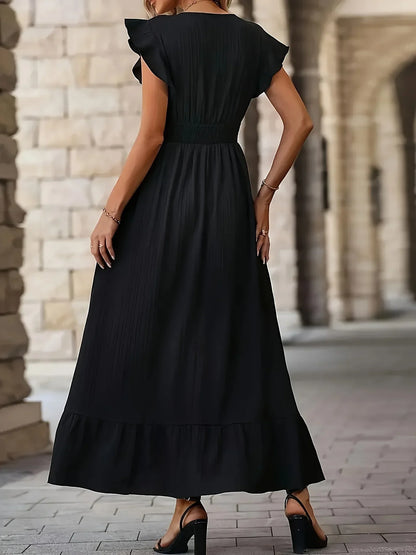 Frau in langem schwarzem Kleid mit Rüschenärmeln, stehend vor Steinmauer, elegantes Abendoutfit.