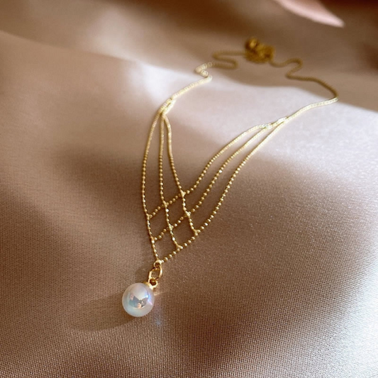 Goldene Halskette mit Perlenanhänger auf beigem Hintergrund, eleganter Schmuck für Damen.