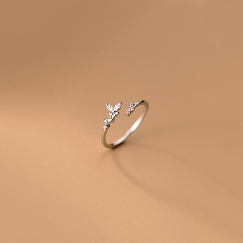 Silberner offener Ring mit Schmetterlingsdesign und Zirkonia-Steinen auf beigem Hintergrund.