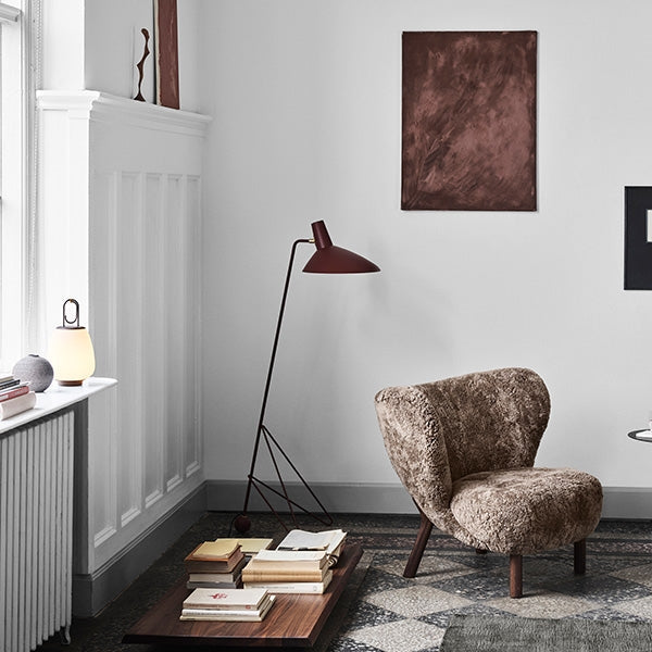 Gemütlicher Lesesessel aus braunem Fellimitat in modernem Wohnzimmer mit Stehlampe und Bücherstapel.