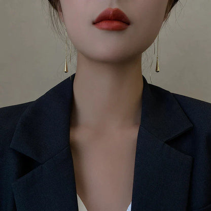 Frau mit goldenen Tropfen-Ohrringen und schwarzem Blazer, eleganter Schmuck, Modeaccessoire.