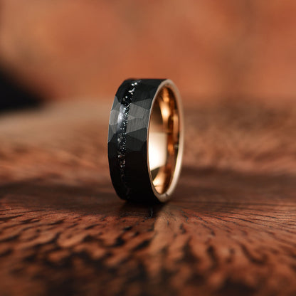 Schwarzer Wolframring mit facettierter Oberfläche und goldener Innenseite auf Holzoberfläche.