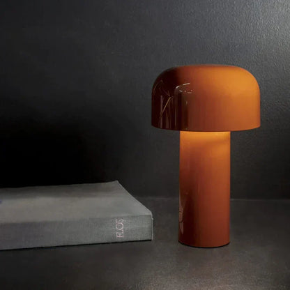 Orange Tischlampe aus Glas auf dunklem Tisch neben grauem Buch, modernes Design.