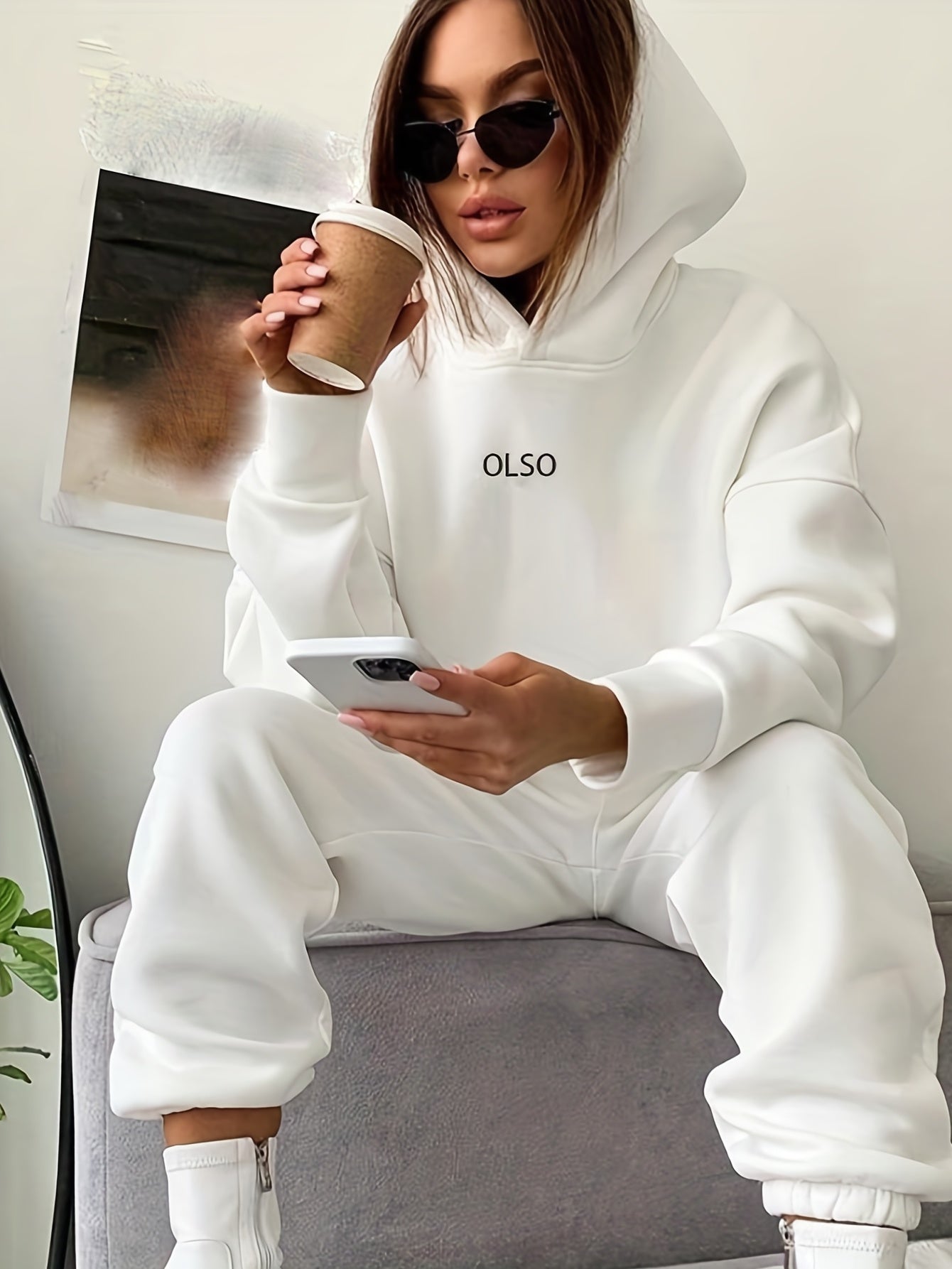 Frau in weißem Hoodie mit Smartphone und Kaffeebecher, modisch, lässig, Sonnenbrille.