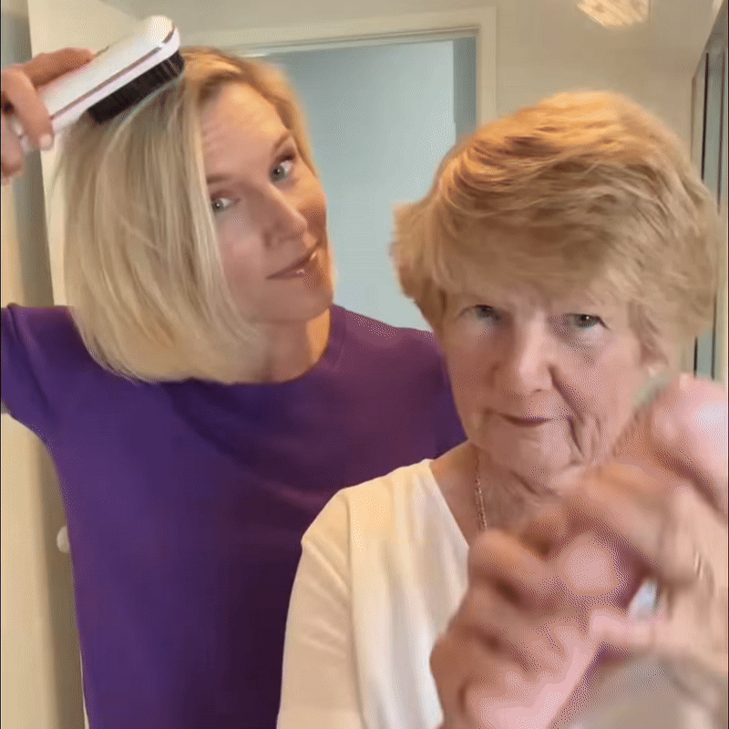 Kvinna i lila tröja borstar sitt blonda hår med en vit värmeborste medan en äldre kvinna med kort hår står framför. 9