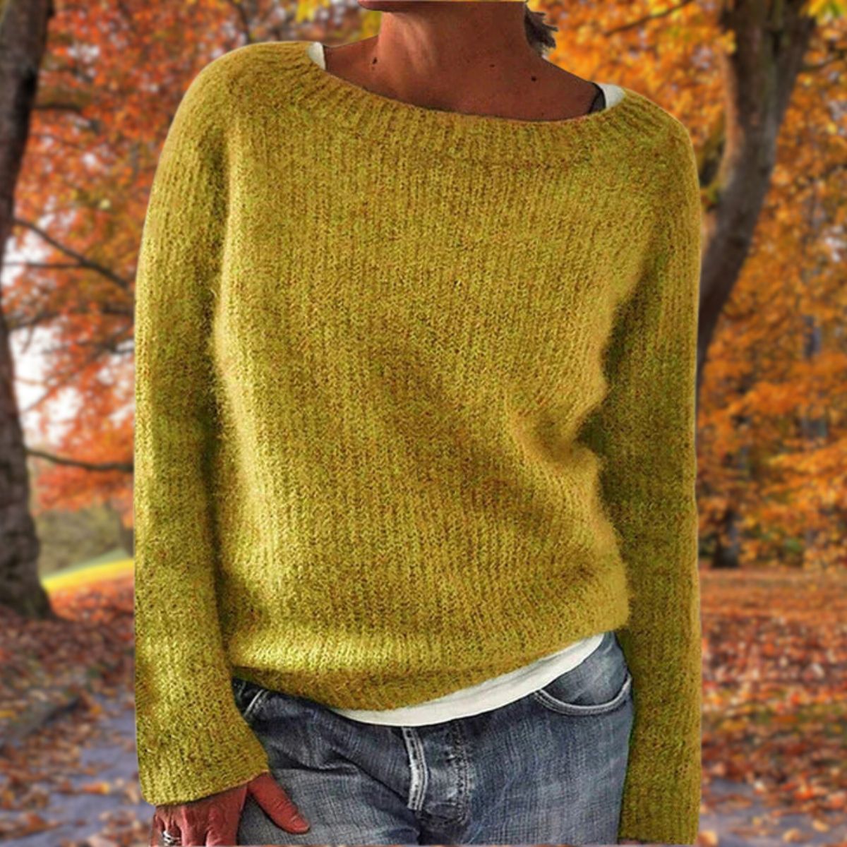 Senapsgul stickad tröja med rund hals och långa ärmar, bärd av en modell över vitt linne och jeans i en höstskog. 1