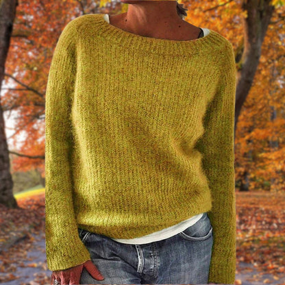 Senapsgul stickad tröja med rund hals och långa ärmar, bärd av en modell över vitt linne och jeans i en höstskog. 1